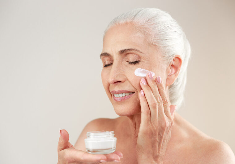 Äldre kvinna som använder ansiktskräm m